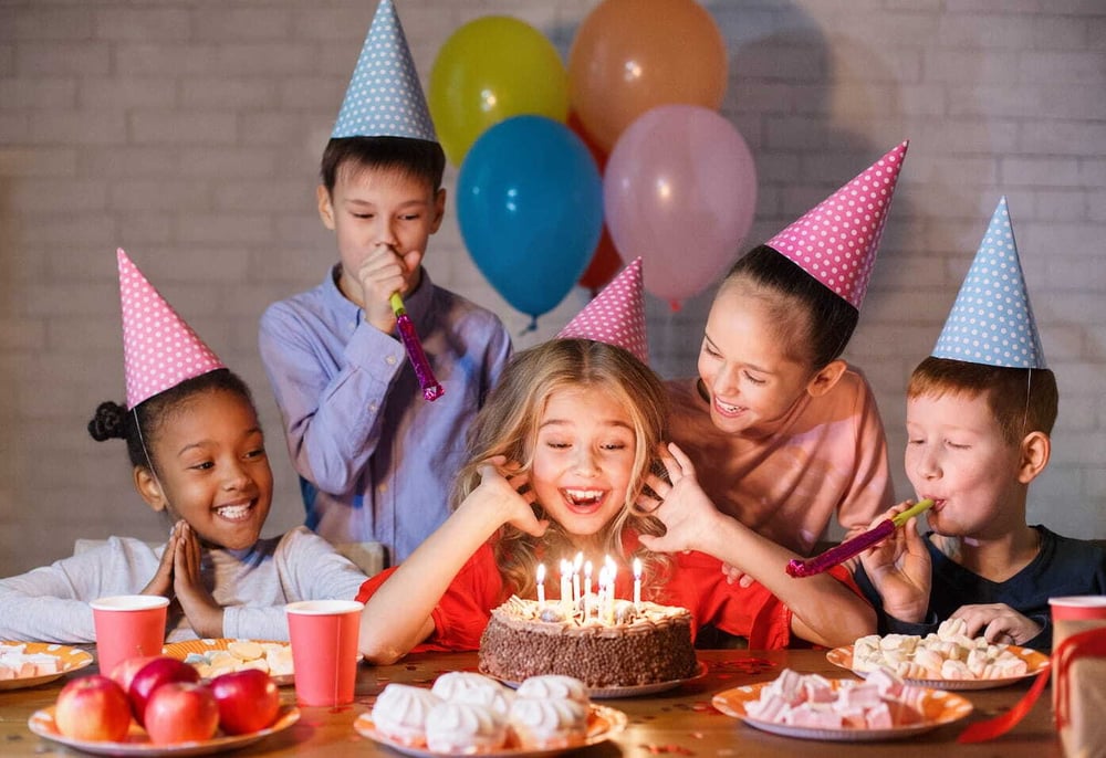 Kids looking at birthday cake with candles, having b-day party